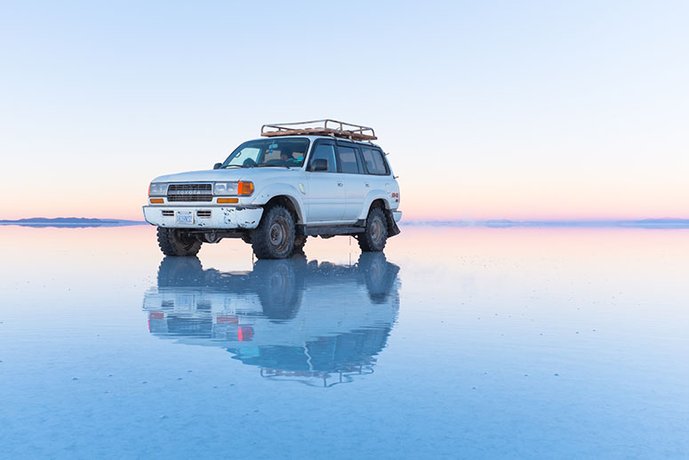 Bil speglar sig i vattnet p Salar de Uyuni..